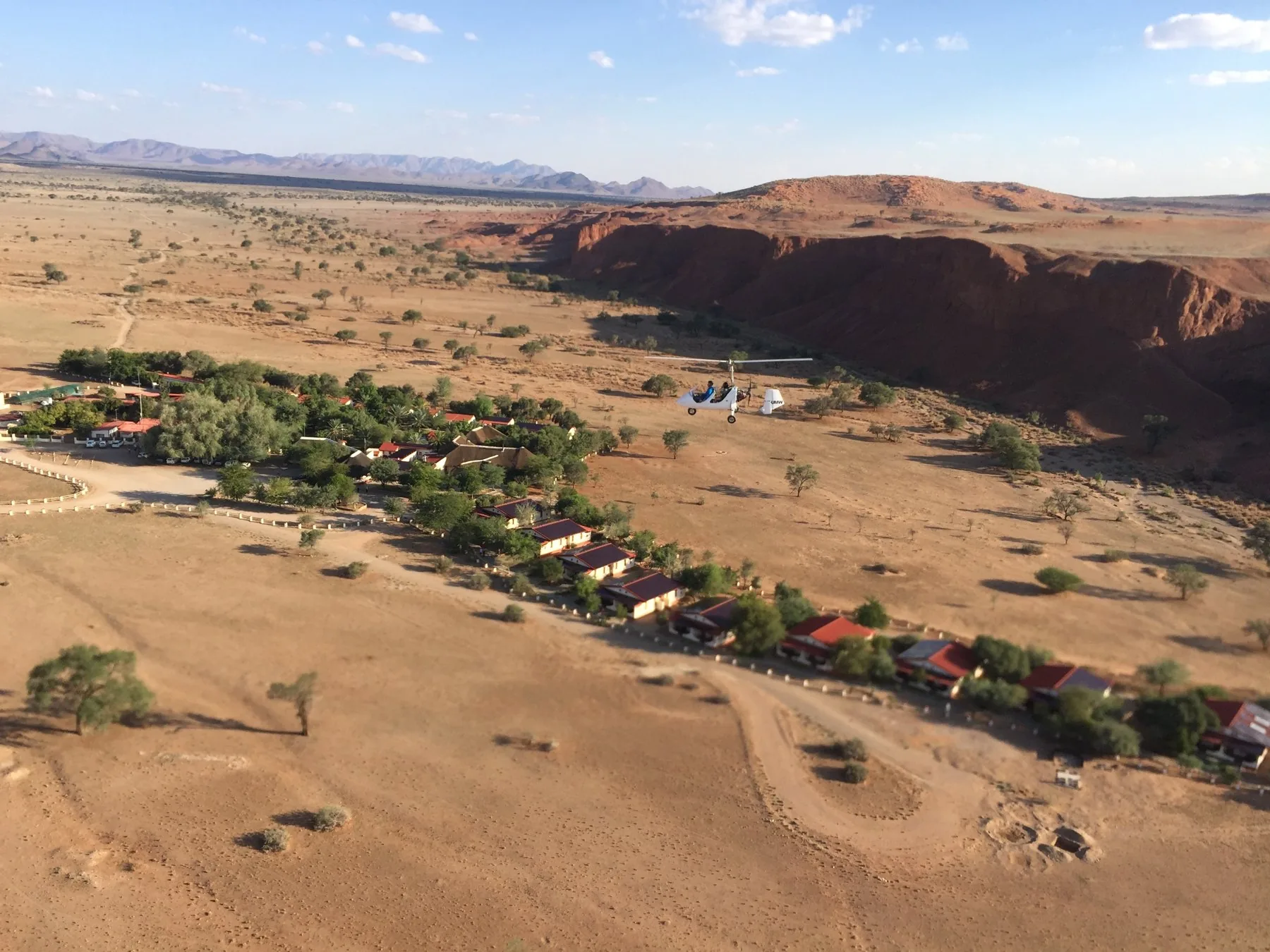 Gyroplane flying above a Namibian lodge beside red cliffs